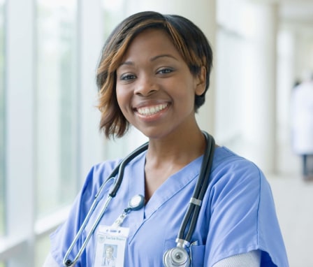 Black female nurse standing in a hospital hallway smiling at the camera.