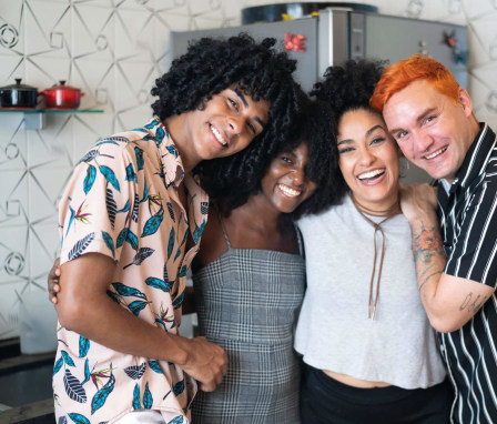 A diverse group of four college friends hug each other while smiling at the camera.