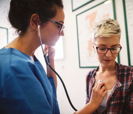 A female nurse using a stethoscope to examine her patient in the clinic.