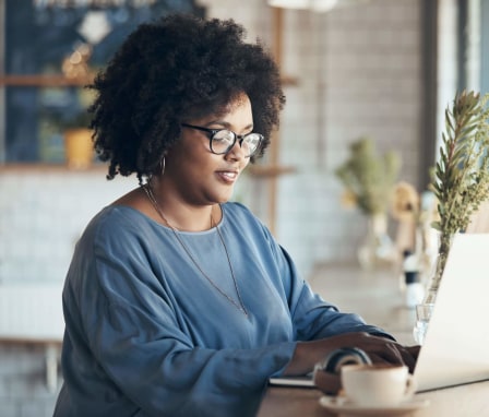 Young African-American female sitting and working on her laptop in a coffee shop during the day.