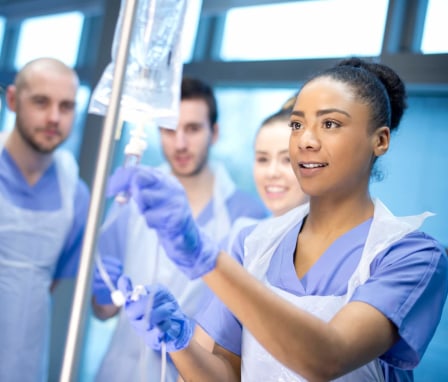 A multicultural group of nursing students practice using the IV drip during an onsite clinical.