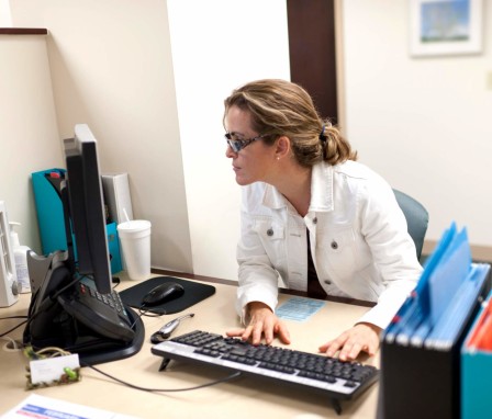 Mid-adult female administrative professional working at her desk in a nursing board office. She is looking at the computer screen while typing on the keyboard.