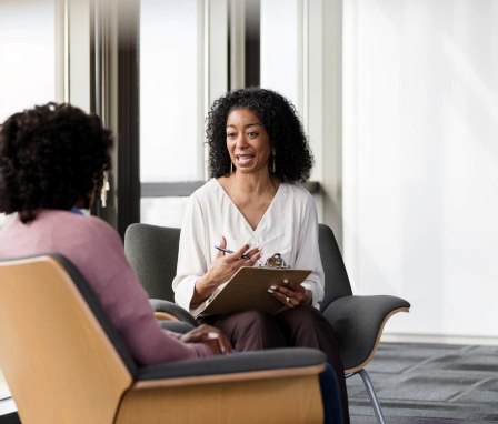 Senior Black female psychiatrist asks a female patient questions about her mental health during a therapy session.