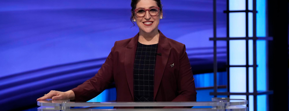 Jeopardy! host Mayim Bialik standing on set