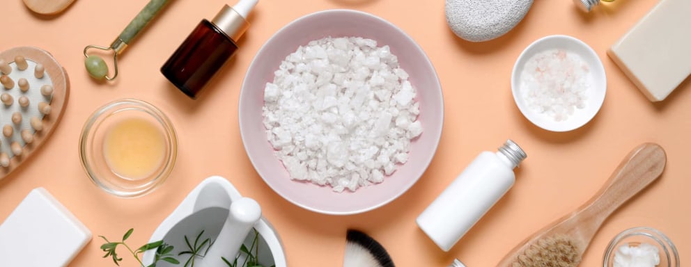 An assortment of personal skincare and cosmetic beauty products for face and body, laid out on a table. The selection includes face serums, brushes, salt scrubs, and moisturizers.