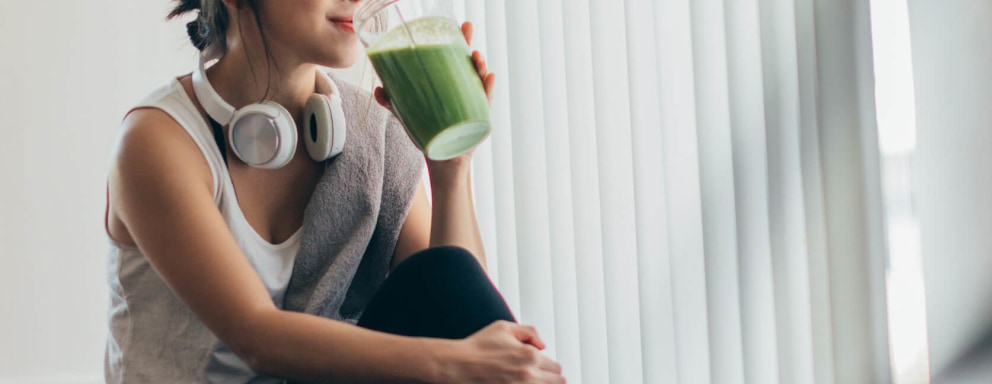 Young woman sitting on her apartment floor drinking a smoothie after a workout.