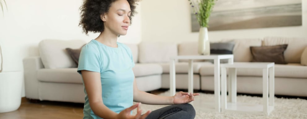 A young African American woman meditating in cross-legged position on her exercise mat in her home.