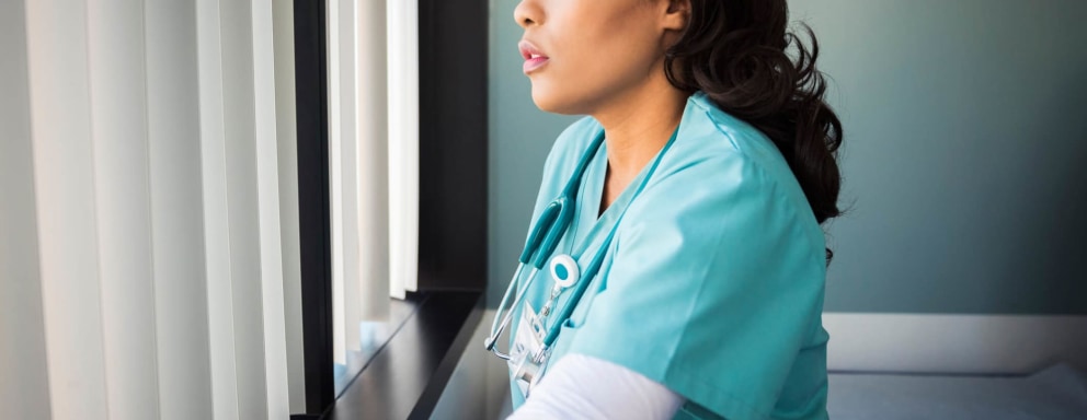 Tired Black female nurse in her 40s is looking out a hospital window.