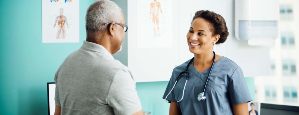 Smiling Black female nurse greets a senior male patient in a family practice clinic.