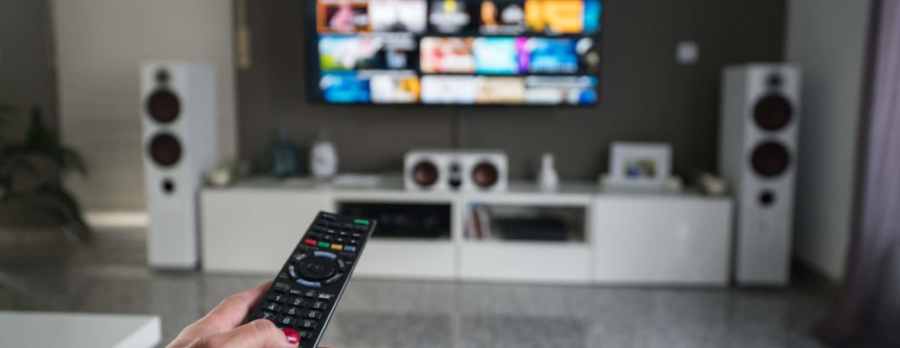 A woman sitting on her living room couch uses her remote to select a TV show.