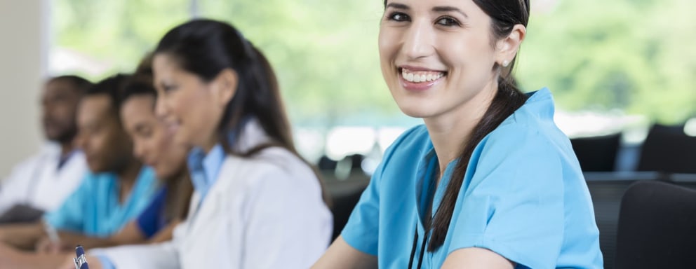 Confident nursing student smiles while taking notes in classroom.