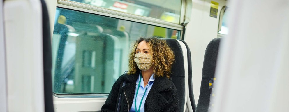 Traveling nurse wearing scrubs and a face mask rides a European commuter train.