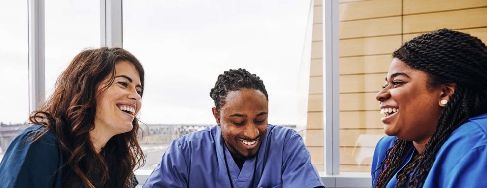 A diverse group of cheerful male and female nurses talking at a table in a hospital during their break.