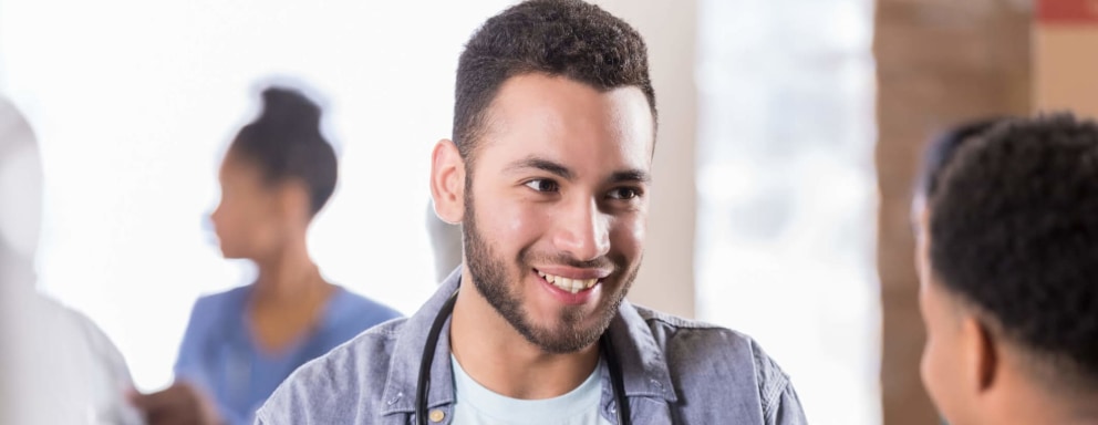 Friendly male nurse working in a community health clinic chats with a teenage client in an arm sling.