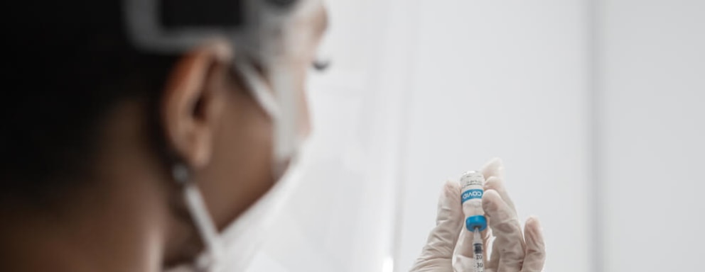 Black female doctor holds syringe and bottle with vaccine for coronavirus. Image Credit: Supamotion / Shutterstock