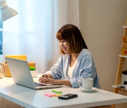 Young Asian-American female student working on completing her college applications on her laptop at home.