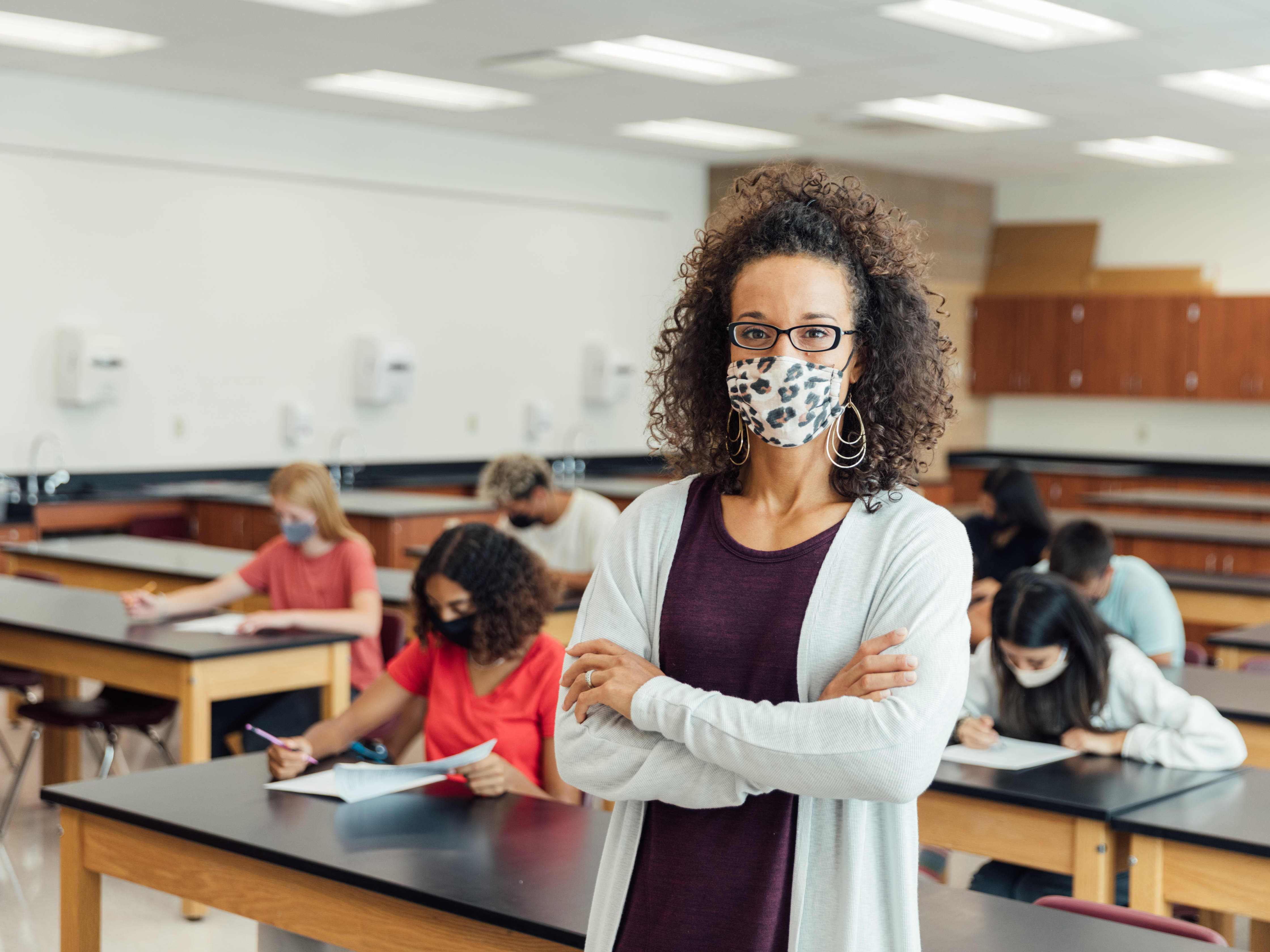Image of teacher in classroom wearing a mask with students behind them