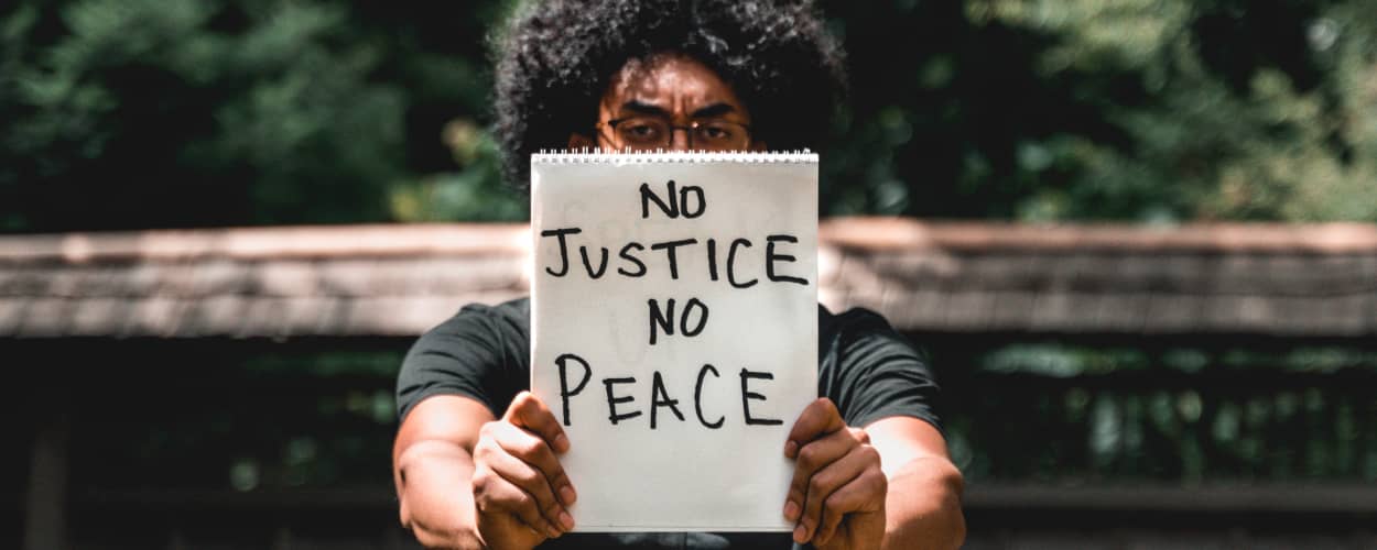Image of a Black person holding a sign reading 'No Justice No Peace'
