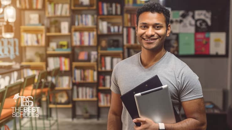 image of young male in library carrying tablet and books