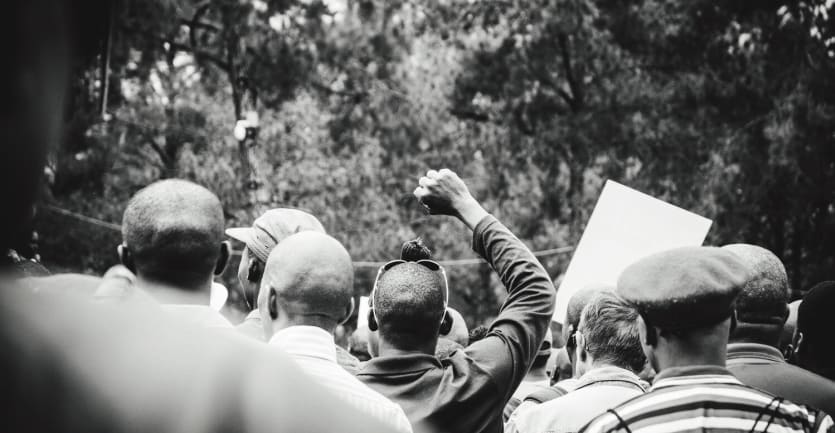 A black-and-white photograph shows a contemporary scene of marching protestors from within the crowd.