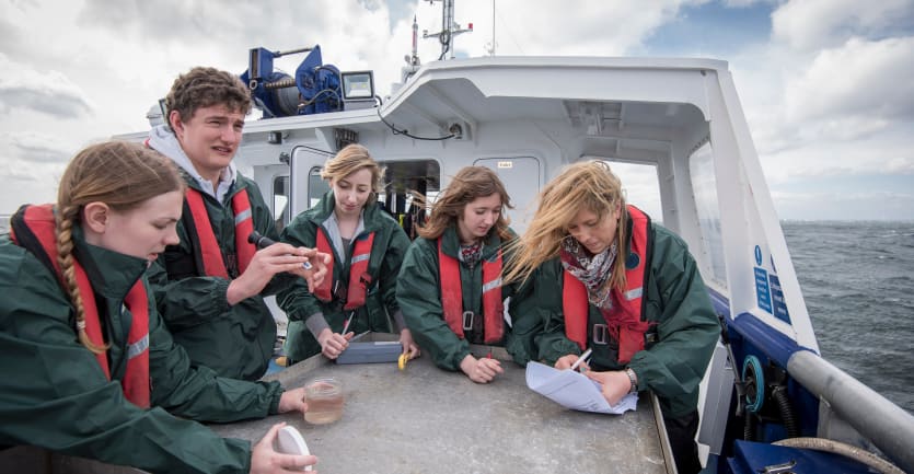 Marine biologist students wearing life jackets sit together on a boat to inspect plankton samples.