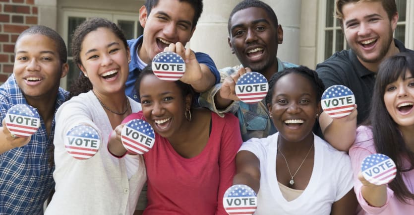 A group of smiling college students face the camera to show off their voting pins.