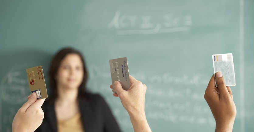 A highlight of several hands holding credit cards thrust up in the air in a classroom.