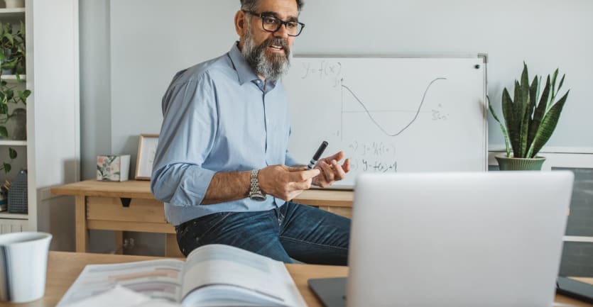 A bearded college professor in glasses and a collared shirt explains a concept via videoconference.