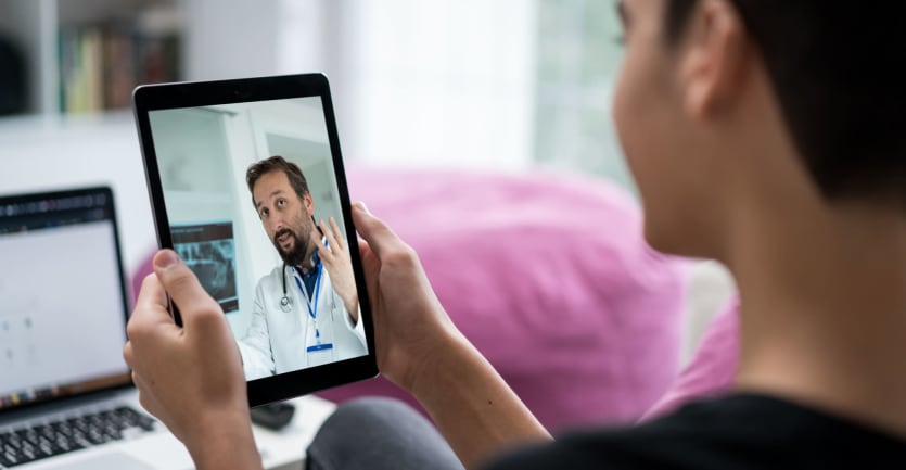 A young man learns from a doctor via video conference on a tablet.