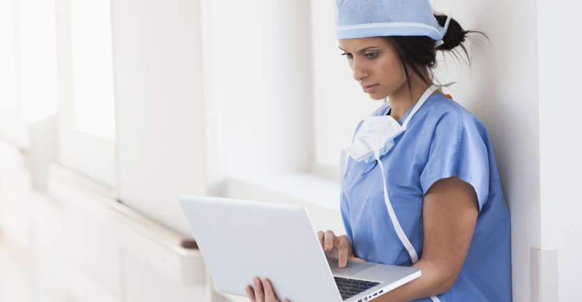 A young surgeon uses a laptop in a hospital.