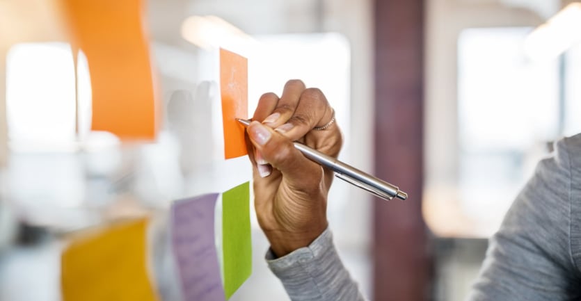 A woman writes on a post-it note that's been stuck to a glass wall in an office.