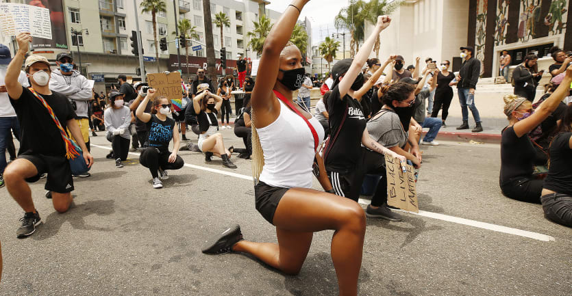 A large group of people made up of mostly college students protests on a street in Hollywood by taking a knee and raising their fists high in the air.