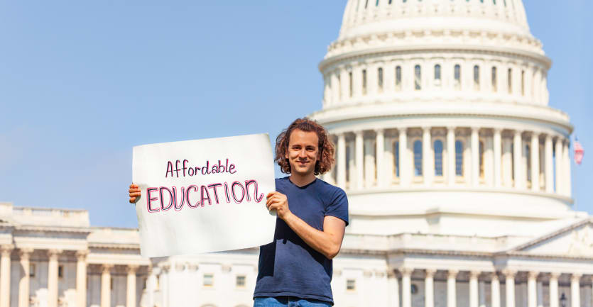 A college student in jeans and a t-shirt holds up a sign that reads Affordable Education while standing in front of the United States Capitol Building on a sunny day.