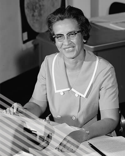 Katherine Johnson smiles while seated at a desk with a typewriter.