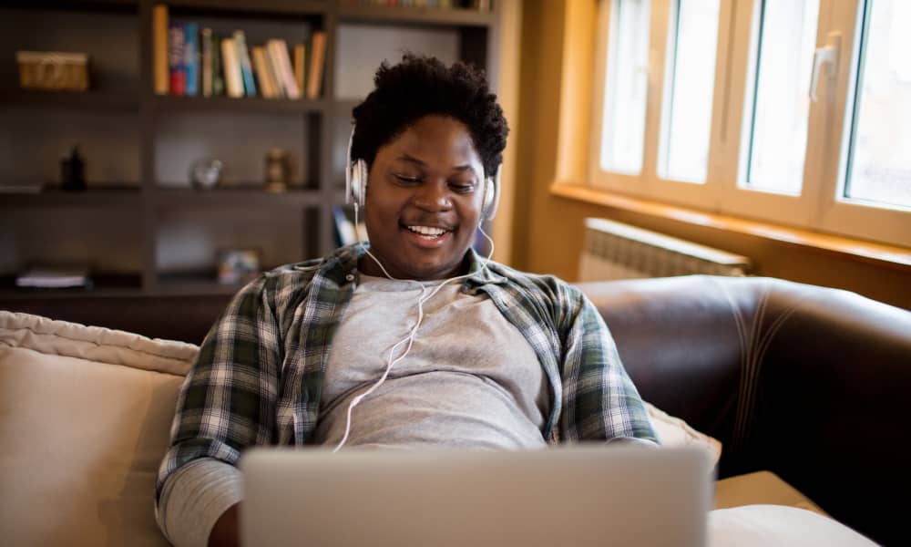 Image of student studying at home on a couch wearing headphones with their laptop in their lap.