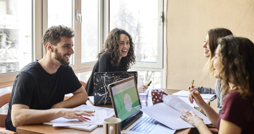 Four students sit at a desk, working together on a project