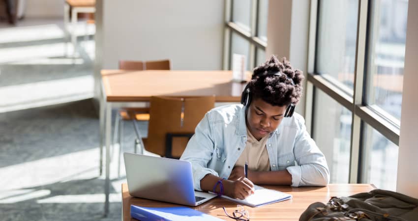 A student with headphones on studies intently at a library desk