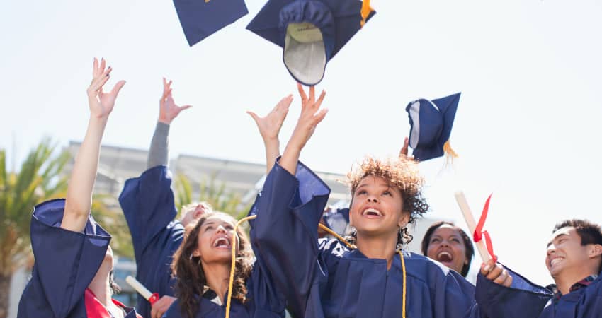 Several graduates in black robes joyously throw their graduation caps into the air