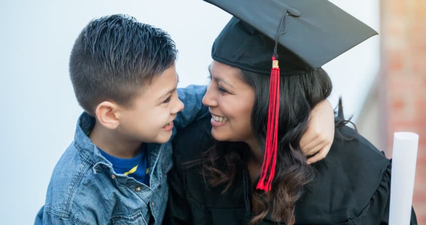 A recent graduate in her cap and gown smiles at her child