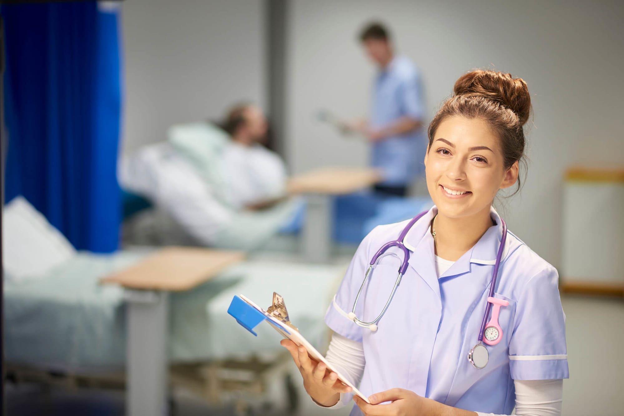 Smiling young female nursing Assistant is holding a clipboard while facing the camera