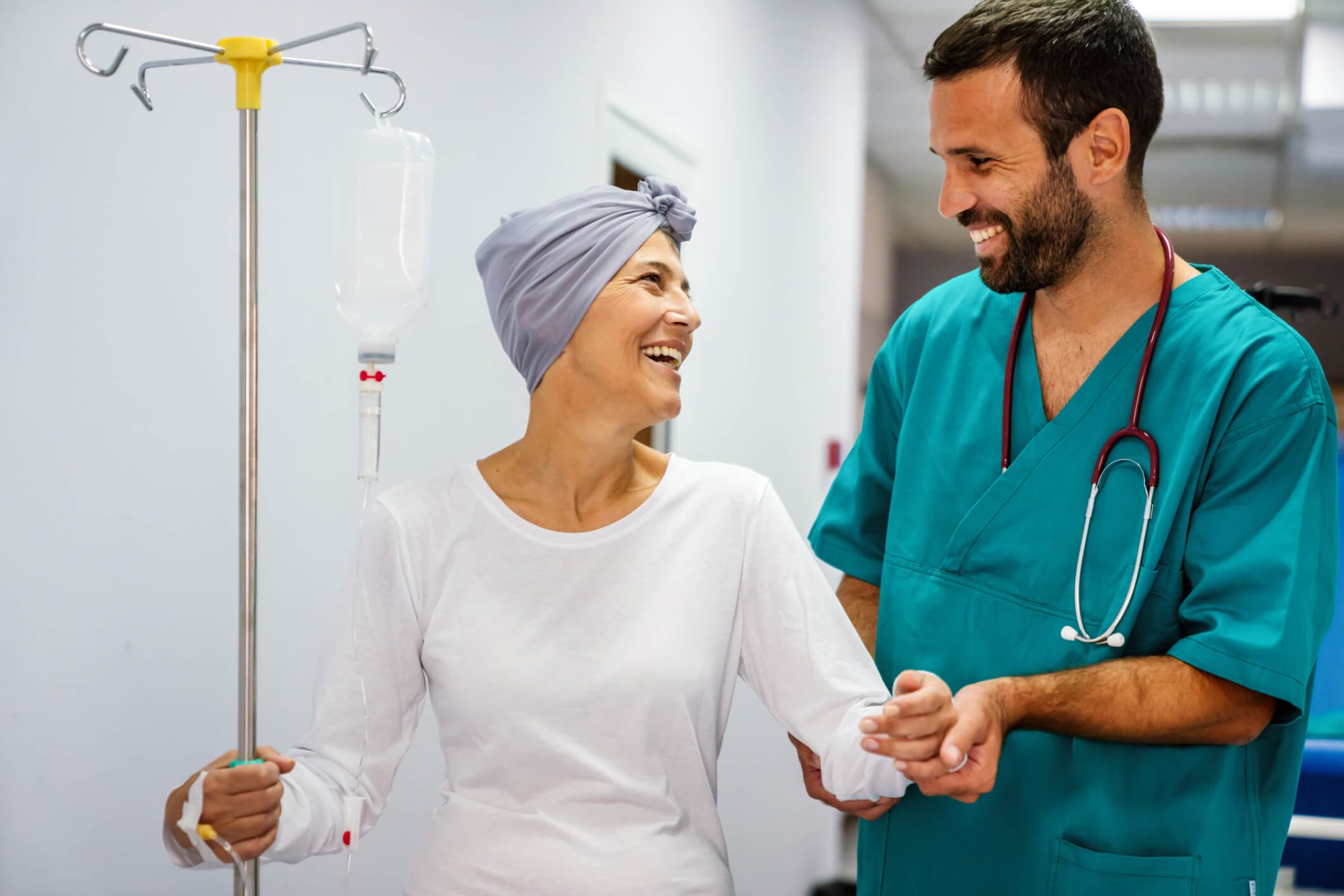 Male nurse assisting an oncology patient as she walks down a hospital hallway.