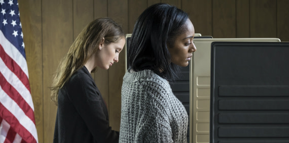 Two millennials voting with an American flag behind them.