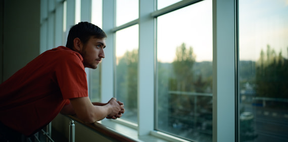 Young person looking sadly and contemplatively out a window.