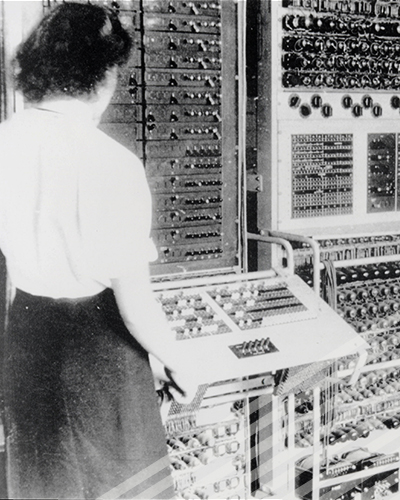One of the Bletchly Park codebreakers eyes a control panel to a very large, early computer.