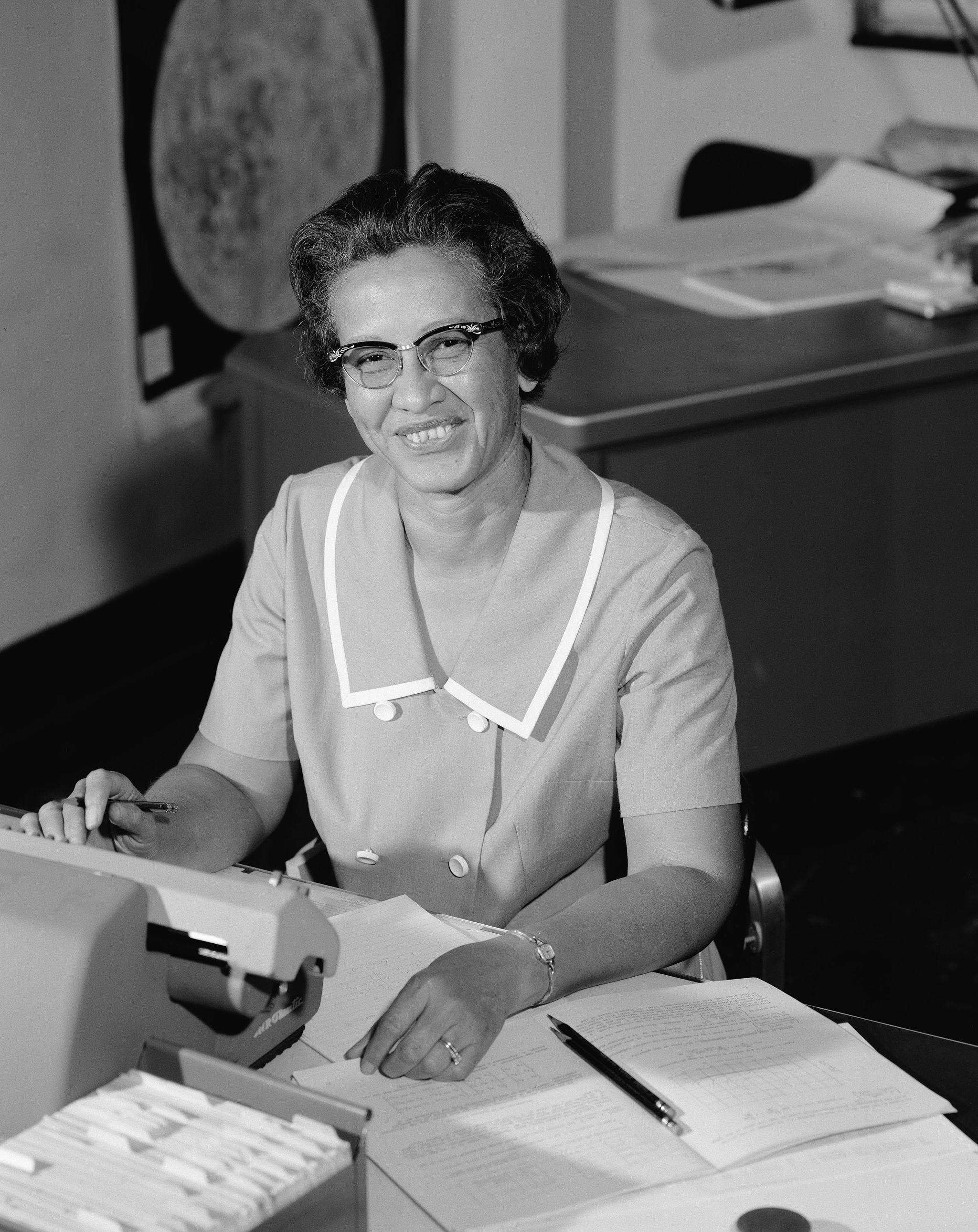 Katherine Johnson smiles while sitting at her desk at NASA.