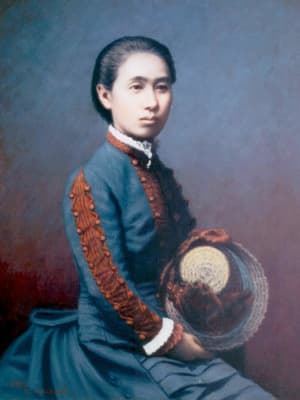 A color photo of Ogino Ginko seated and looking away from the camera, holding her hat in her hands
