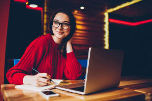 Young woman in knit sweater, working on laptop by a window