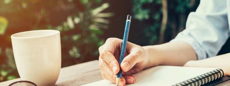 Person writing in notebook with coffee nearby