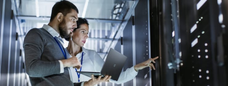 Bearded man with laptop and a woman conferring near computers