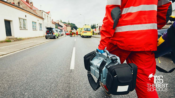 The Best Online Emergency Management Degree Programs Hero Image:
The 15 Best Online Bachelor's in Emergency Management Programs (image of an emergency medical technician striding toward the scene of an accident on the road of a small village)